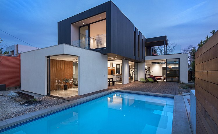 Exterior view at dusk of contemporary style house with swimming pool and deck and view of b3 kitchen inside the very open plan architecture.